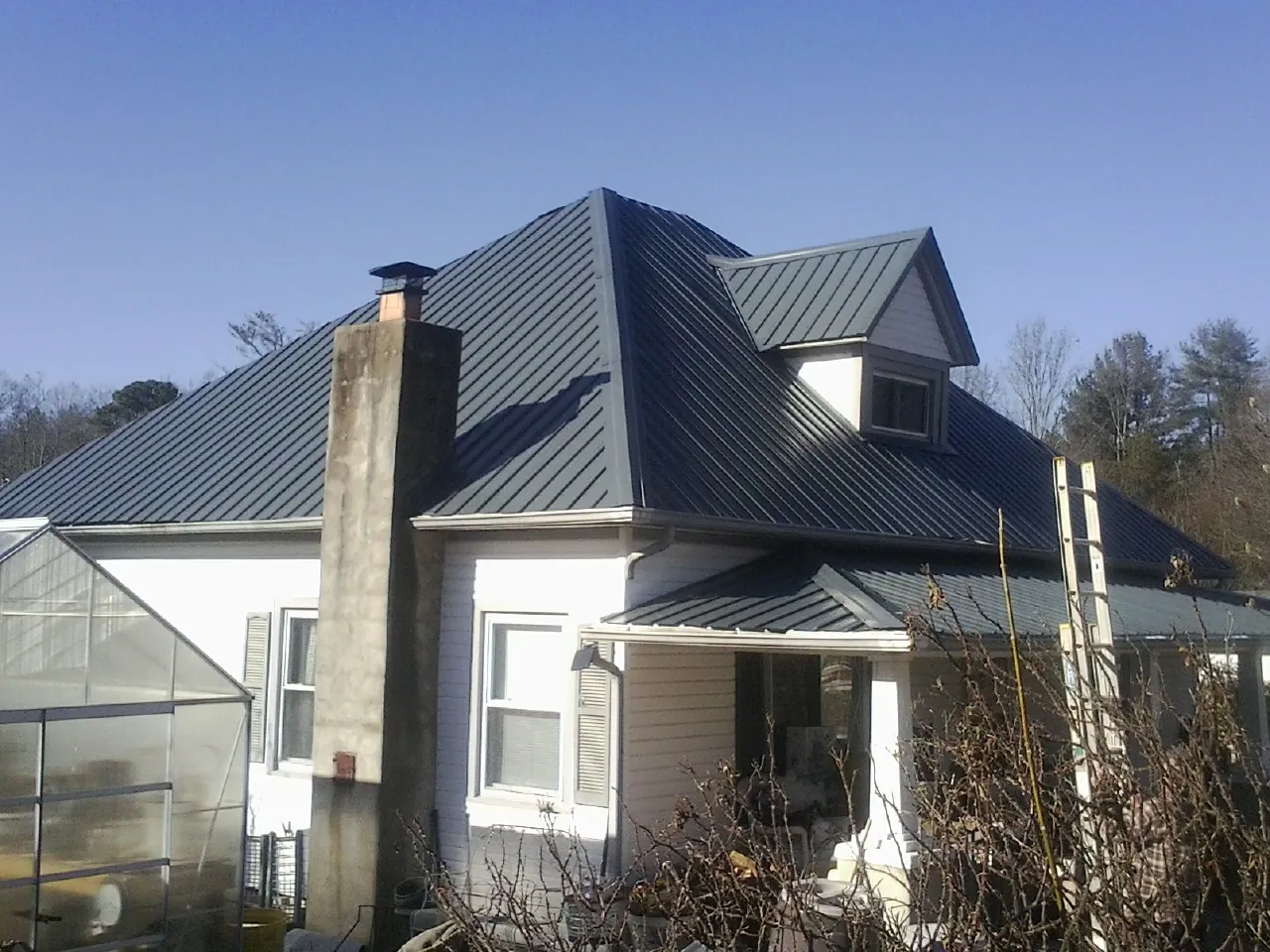 Dark blue standing seam metal roof on a white farmhouse with dormer — Slate & Tile Roof Repair by Roofing Brothers in Cornville