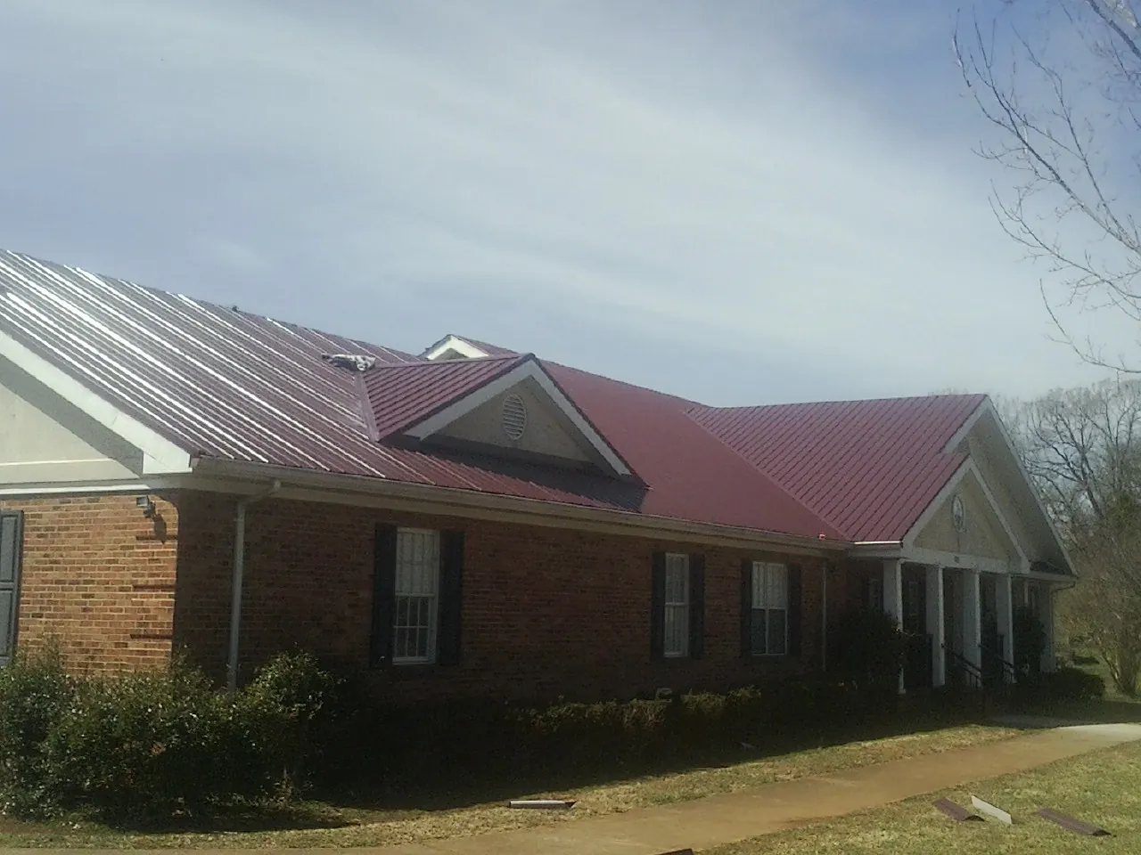 Red metal roof with gabled entries on a long brick building, from a Hail Damage Roof Repair job in Cornville