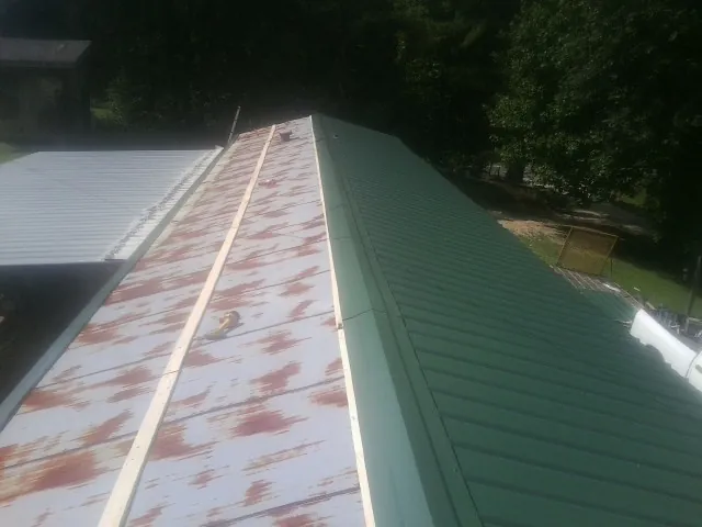 Old rusted panels beside newly installed green metal roofing — Wind Damage Roof Repair by Roofing Brothers in Cornville