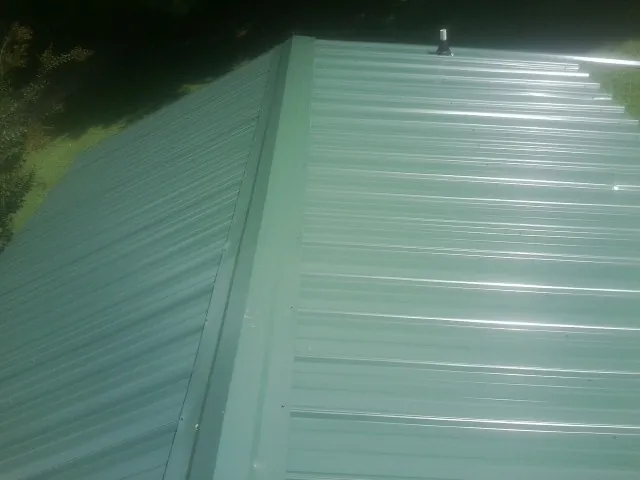 New green metal panels meeting at the ridge of a roof — Flat Roof Repair work by our crew in Cornville