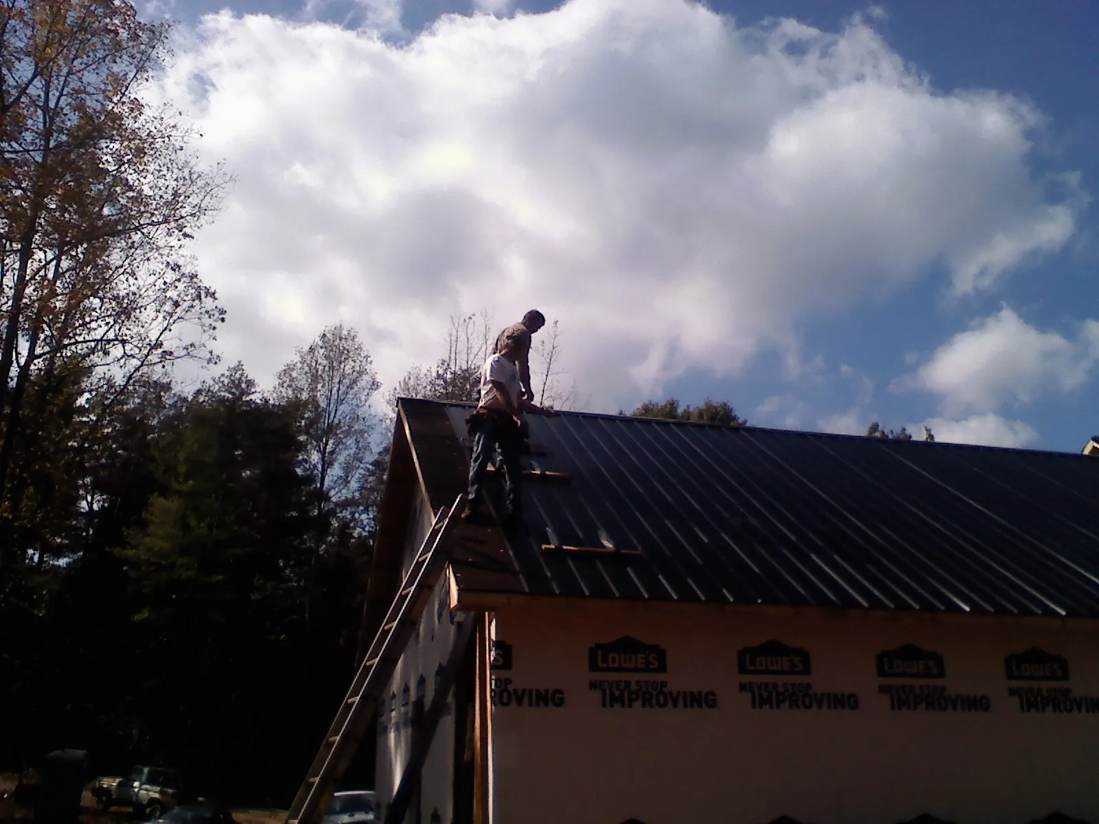 Roofer fastening dark metal panels high against a cloudy sky, from a Roof Inspection job in Cornville
