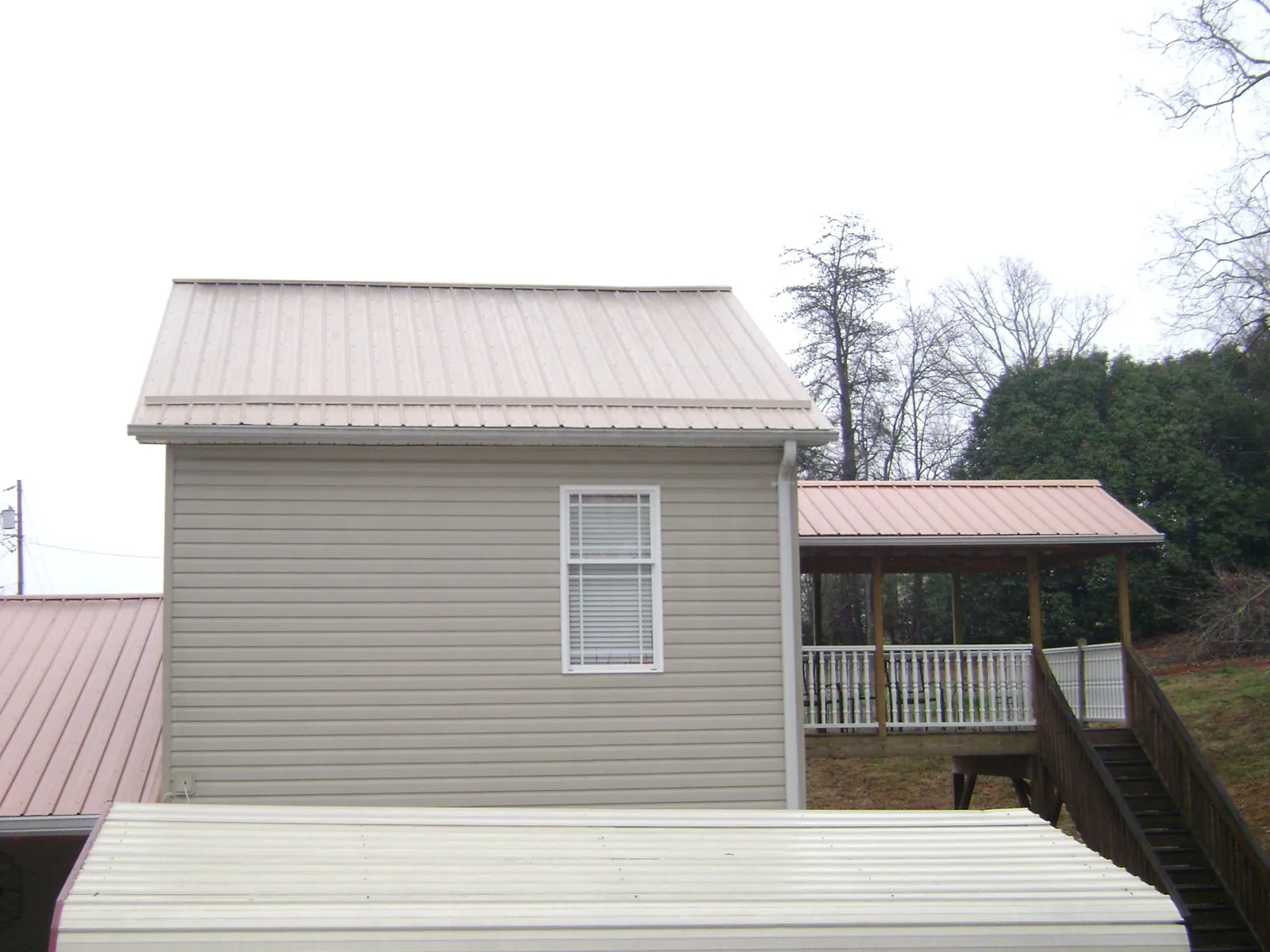 Tan metal roofs on a two story addition and attached porch, from a Roof Replacement job in Cornville